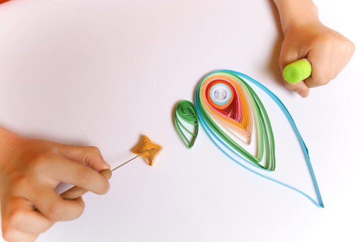 a child in an orange T-shirt shows twisted paper strips in the quilling technique. the boy prepared the blanks for gluing them to the paper