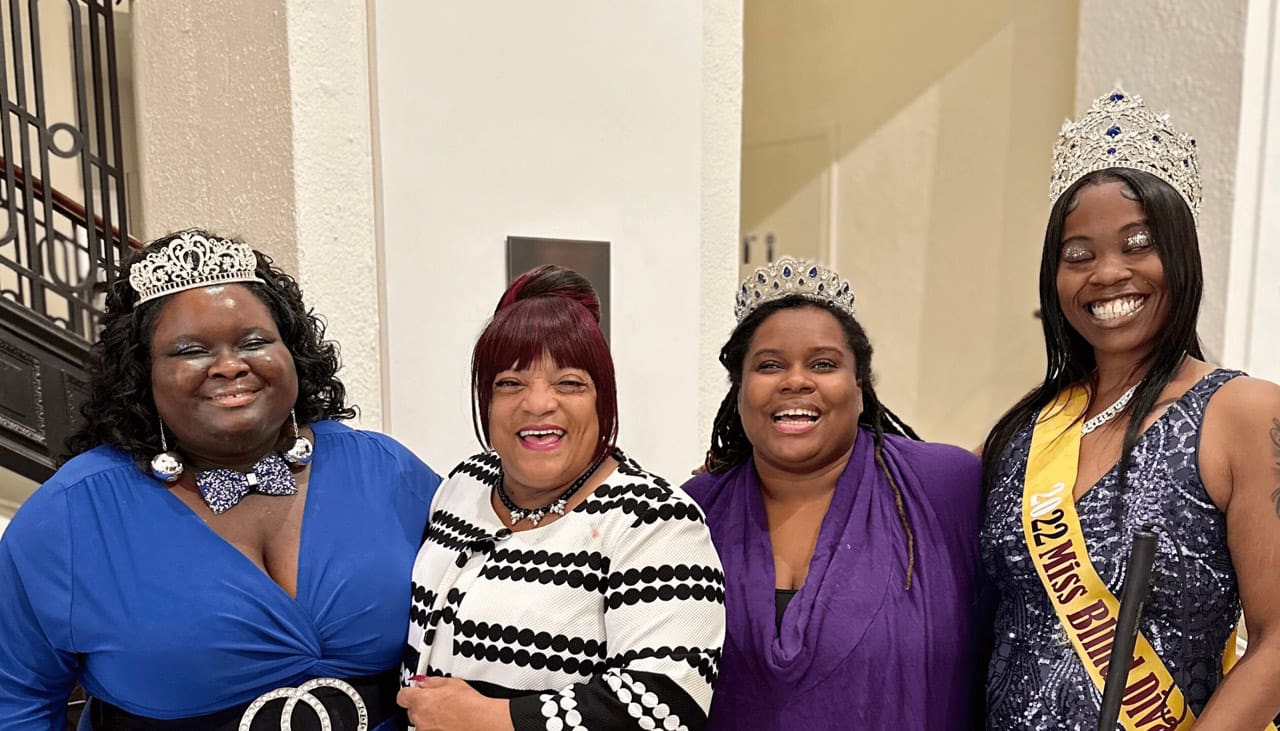 four women smiling and standing by a yellow table