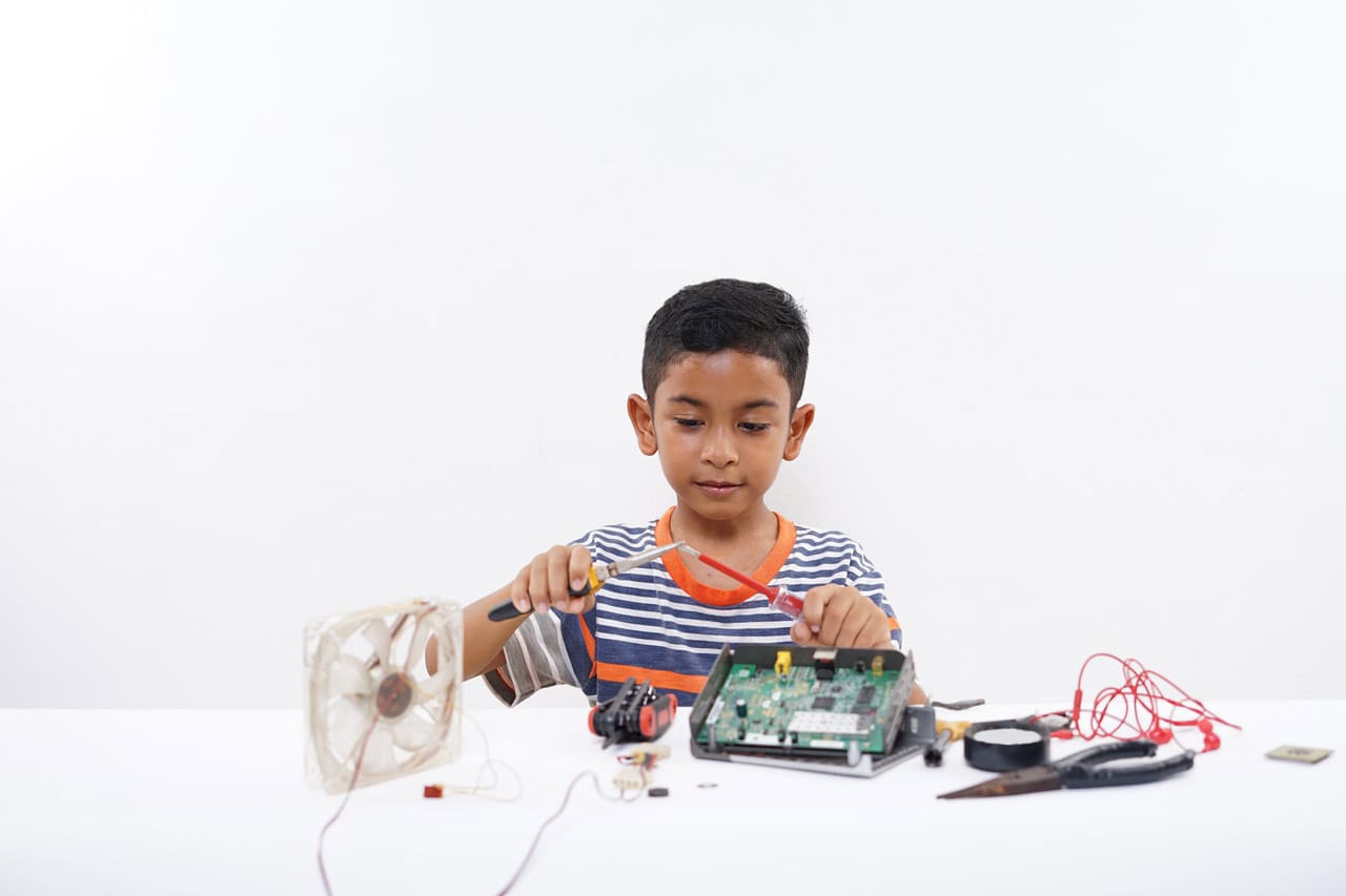Asian schoolboy electrician repairing computer part at home