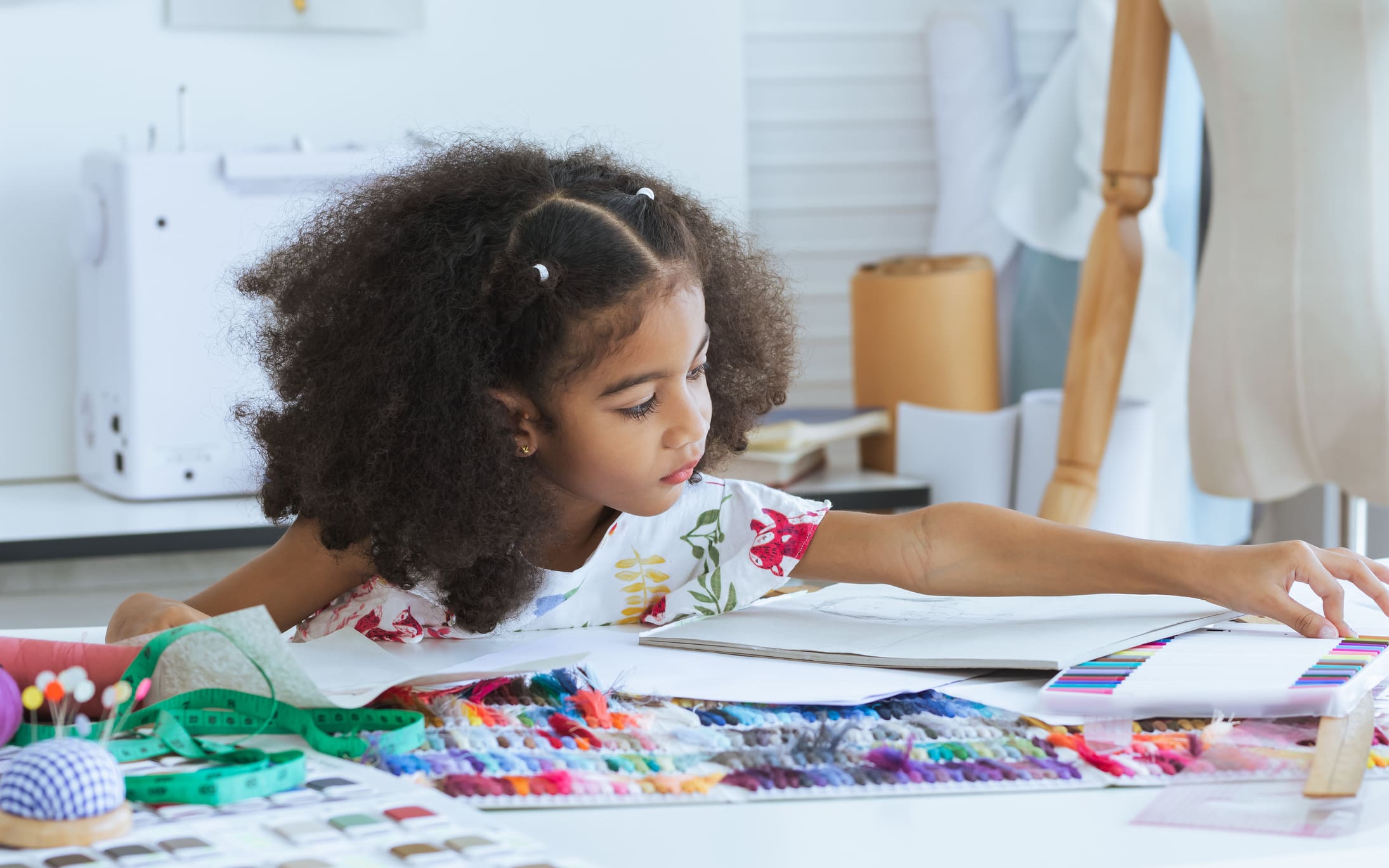 Cute African little girl drawing or sketching clothing design on paper at tailor room, cozy home as her career dream, smiling with happiness and fun. Leisure, Lifestyle, Education, Kid Concept
