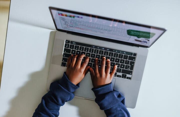 Young black student learning to code in a computer science classroom. High angle view of a kid typing on a laptop as he works on a programming exercise in a digital literacy lesson.